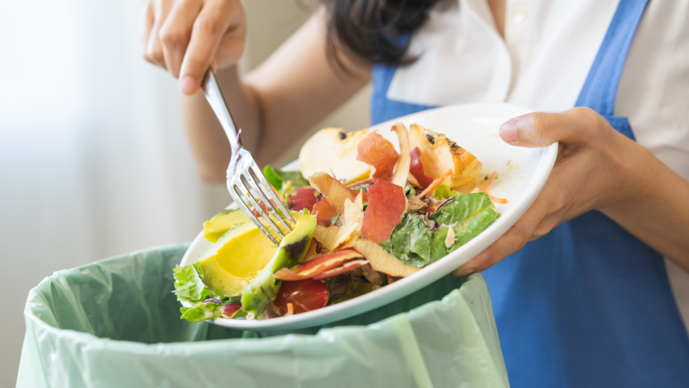 Compost from leftover food asian young housekeeper woman, female hand holding salad bowl use fork scraping waste, rotten vegetable throwing away into garbage, trash or bin. Environmentally responsible